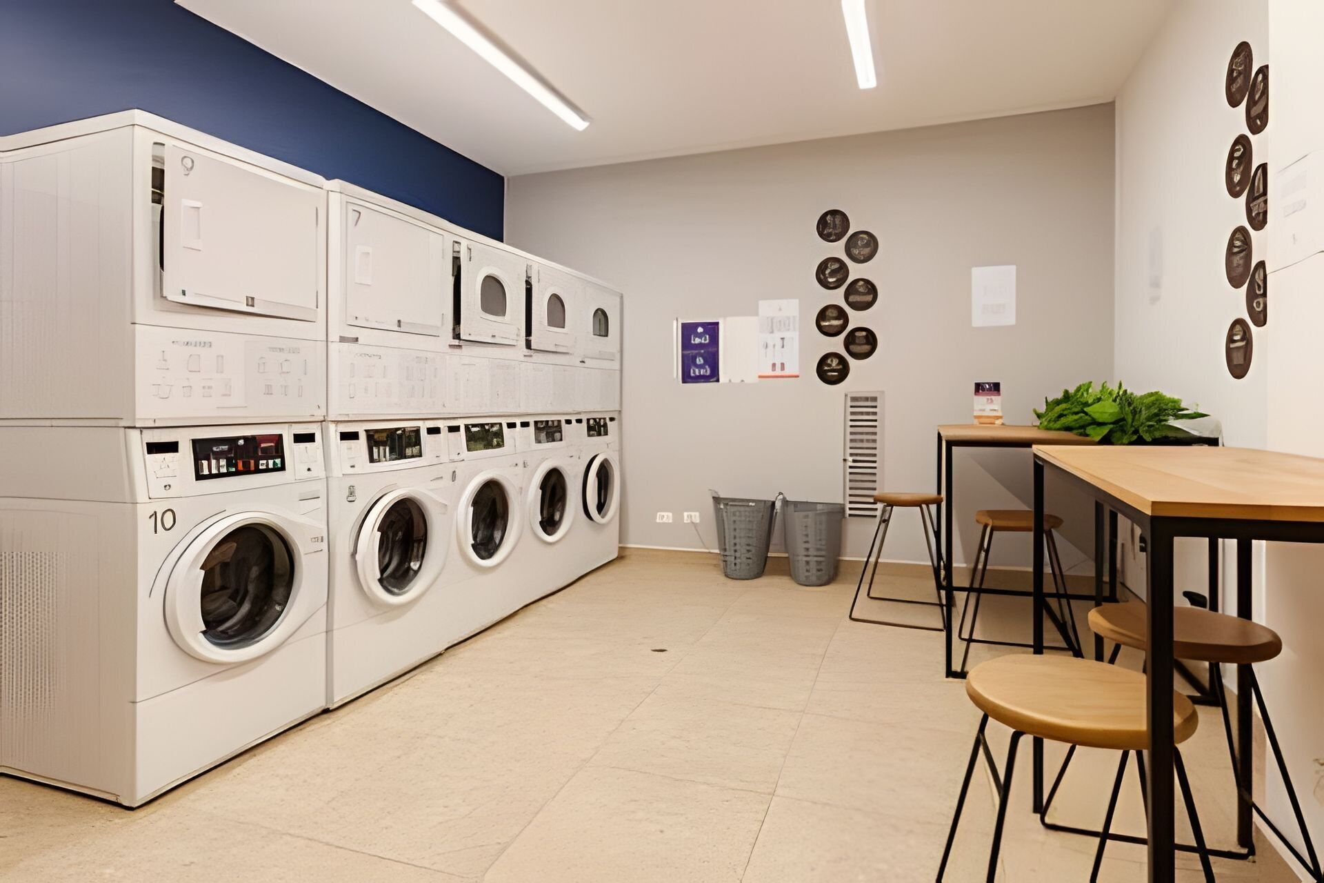 A laundry room with stacked washers and dryers, a table with chairs, and a trash can.