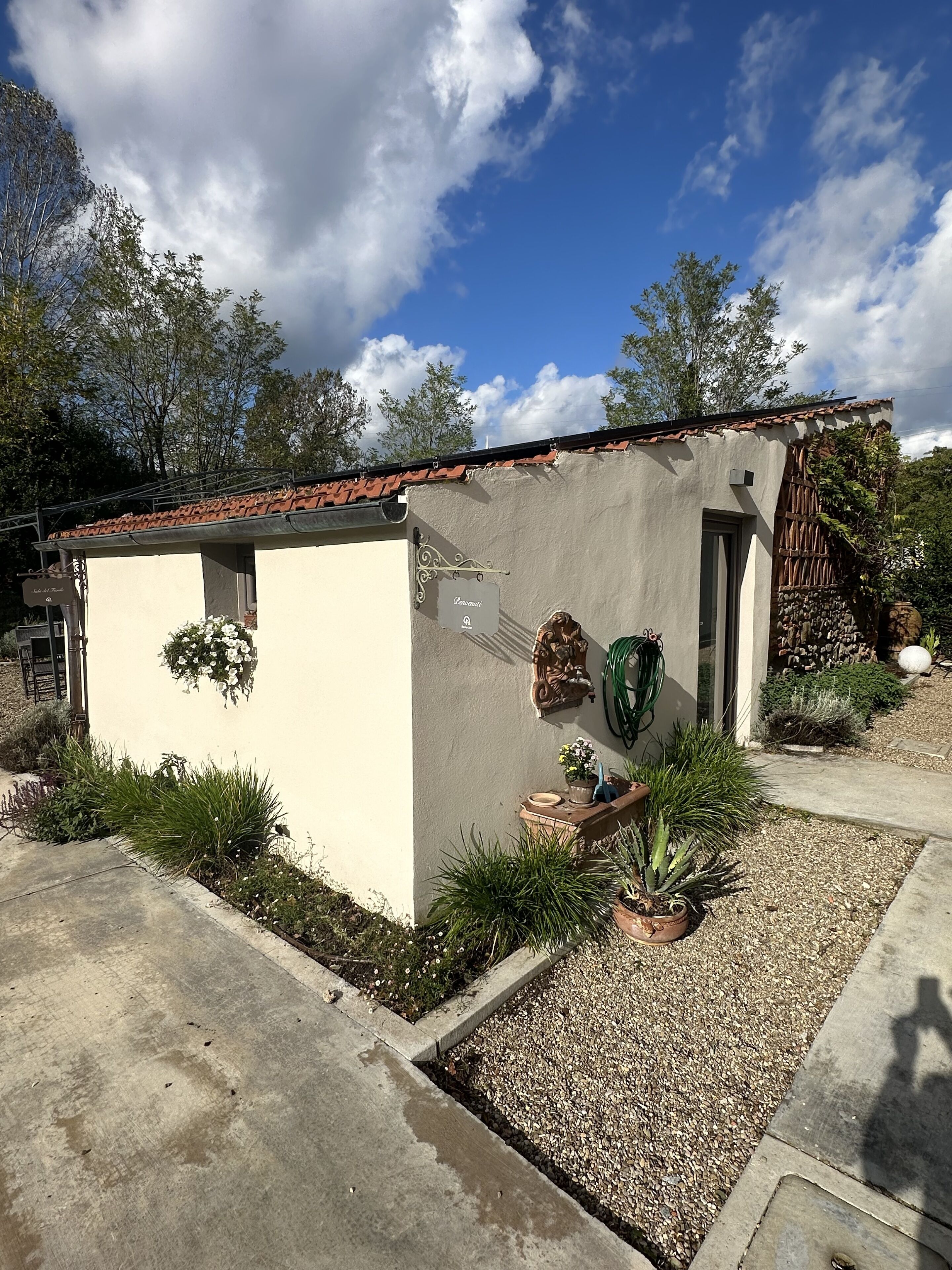 A small building with a tiled roof, a door, and a window. There are potted plants and a garden area with gravel.