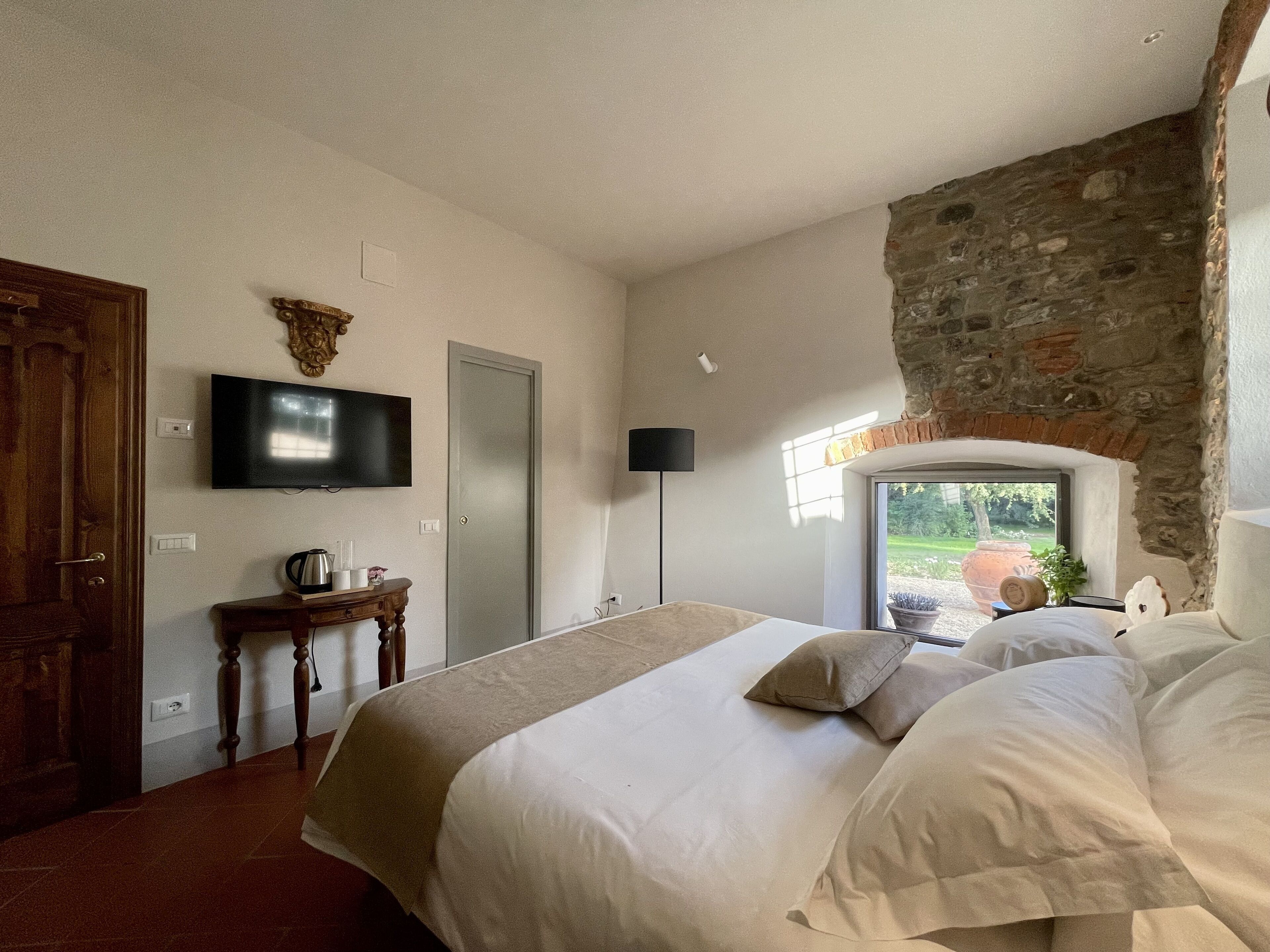 Un dormitorio con cama, televisor en la pared, una puerta y pared de piedra.