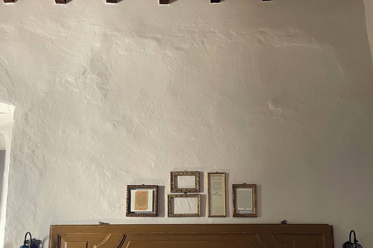 Un dormitorio con cabecera de madera, cama con ropa de cama blanca y beige, y diplomas enmarcados en la pared.