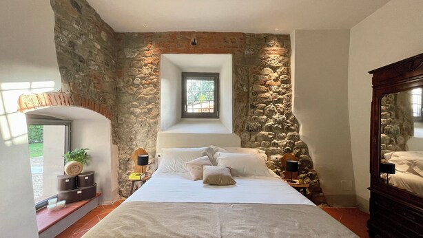 Ein Schlafzimmer mit Steinwand, Bett, Nachttisch, Fenster und Spiegel.