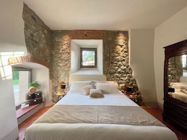 Un dormitorio con pared de piedra, una cama, una mesita de noche, un ventanal y un espejo.