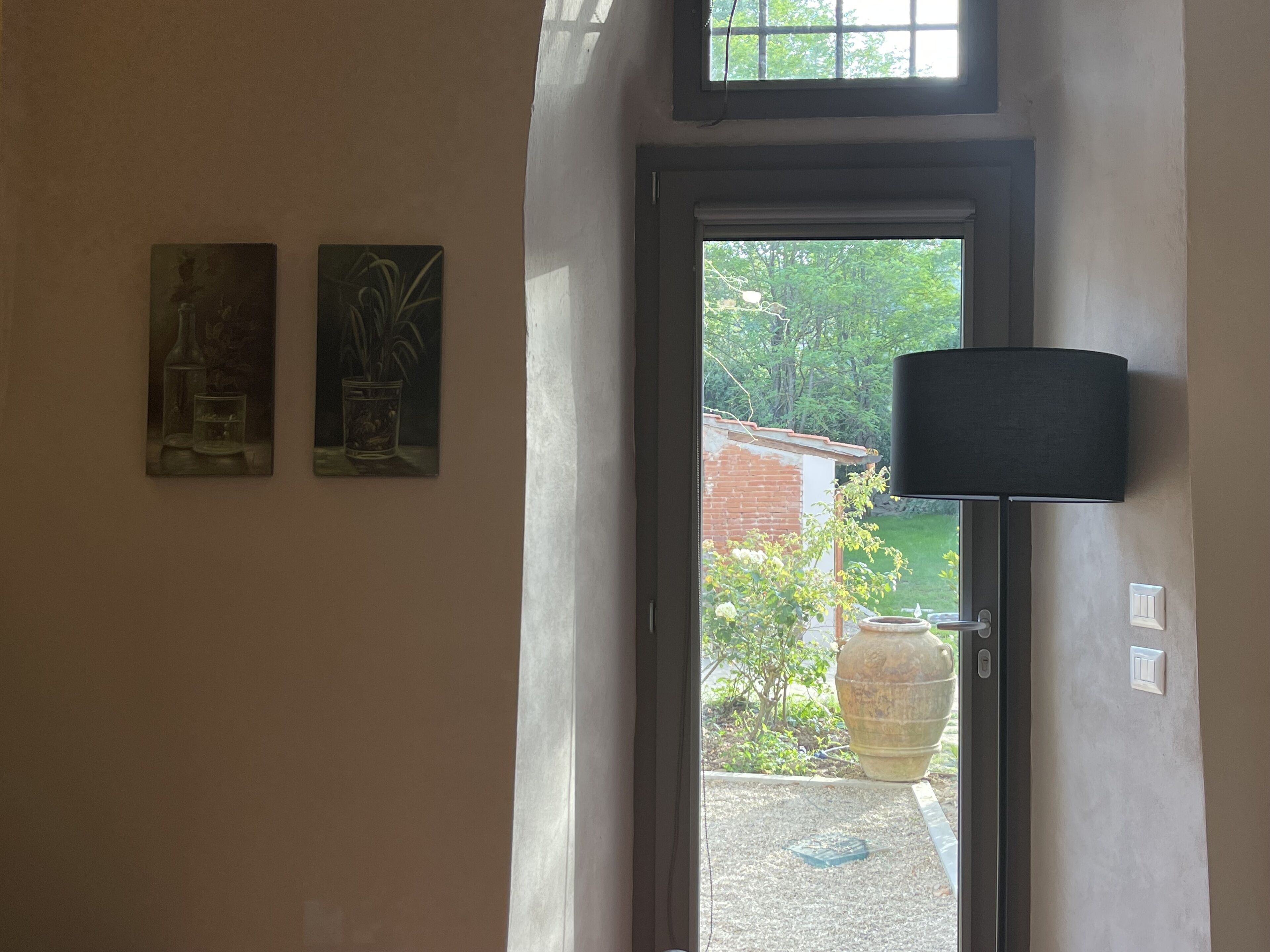 A doorway with two paintings on the wall, a large potted plant outside, and a lamp to the right.
