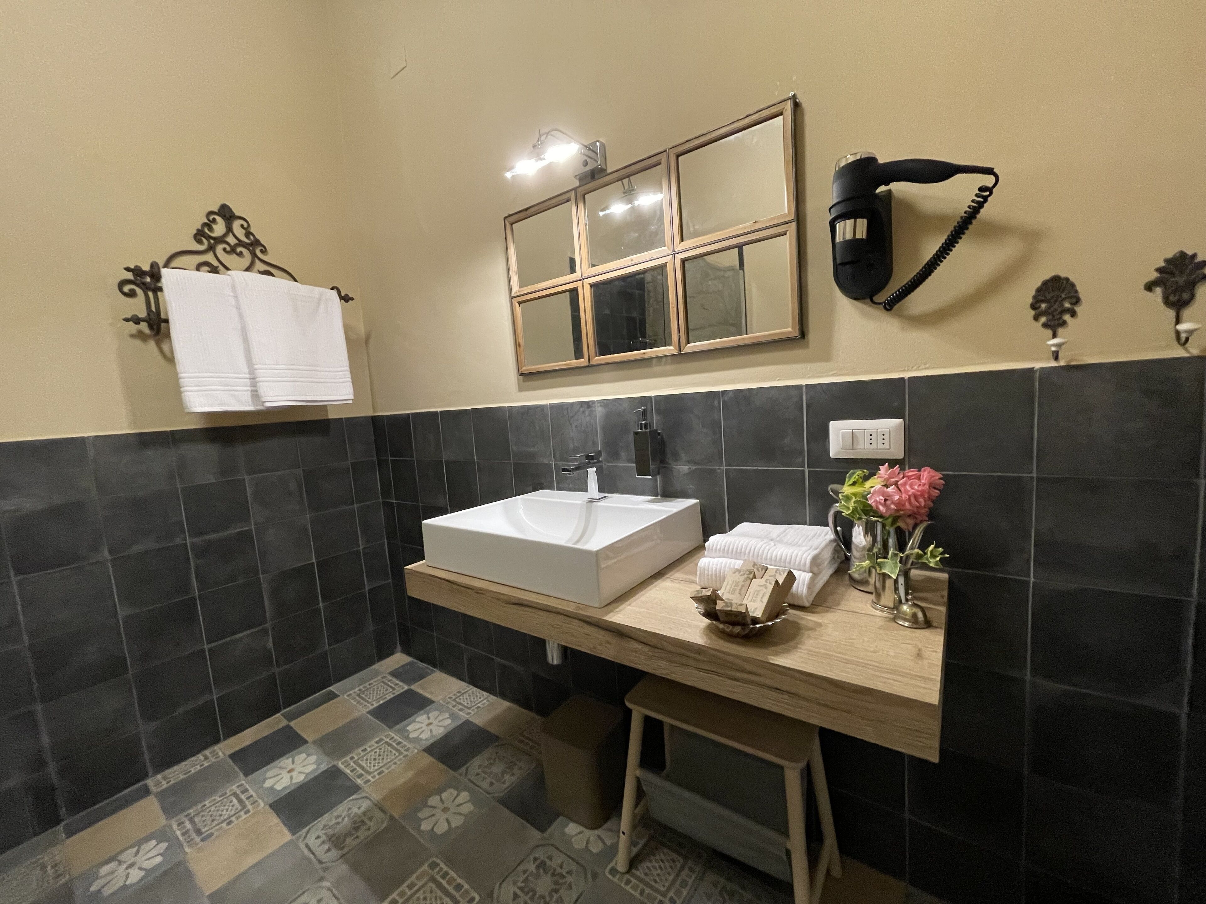 Une salle de bain avec un lavabo blanc, des murs recouverts de carreaux foncés, un miroir et un porte-serviettes.