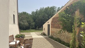 Eine Terrasse mit Kiesweg, Holzstühlen und einem Tisch. Im Hintergrund ein Gebäude mit einer Steinwand und einer Tür.