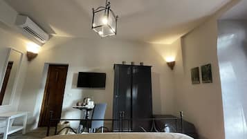 Habitación de hotel con cama, escritorio, silla, televisor, armario y lámpara colgante.