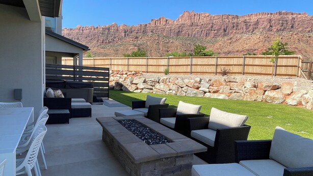 An outdoor patio with a stone fire pit, wicker furniture, and a view of a rocky mountain range. - Beautiful New 4 Bedroom Home with views Minutes from Arches (Moab)