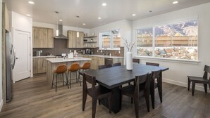 A modern kitchen with wooden cabinets, a central island, and a dining area with a dark wood table and chairs. - Beautiful New 4 Bedroom Home with views Minutes from Arches (Moab)