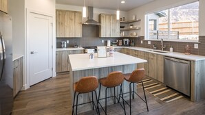A modern kitchen with a central island, bar stools, wooden cabinets, and a large window. - Beautiful New 4 Bedroom Home with views Minutes from Arches (Moab)