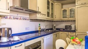 Una cucina compatta con piano di lavoro blu, mobili bianchi, un forno a microonde, una macchina per il caffè e un'lavastoviglie.