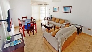 A living room with a sofa, a coffee table, a TV, and a dining area with chairs and a table.
