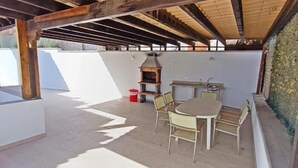 An outdoor patio with a wooden pergola, a barbecue grill, and a table with chairs.