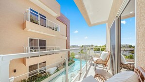 Un edificio moderno con balcón de vidrio, piscina y mobiliario exterior.