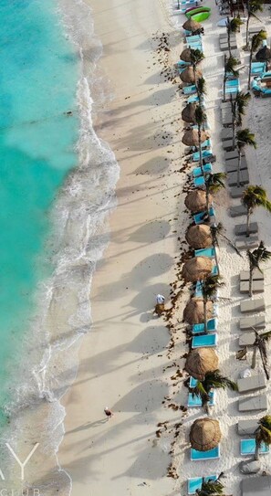 An aerial view of a beach with rows of sun loungers and thatched umbrellas, a clear turquoise sea, and a sandy shore. - Villa Aaktun PGA Tulum (Tulum)