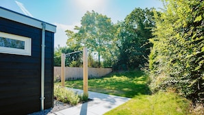 A modern house with a dark wooden exterior, a visible window, and a paved pathway leading to a grassy yard. - Modern Holiday Home With Spacious Garden and Terrace Suitable for 5 People (Ouddorp)