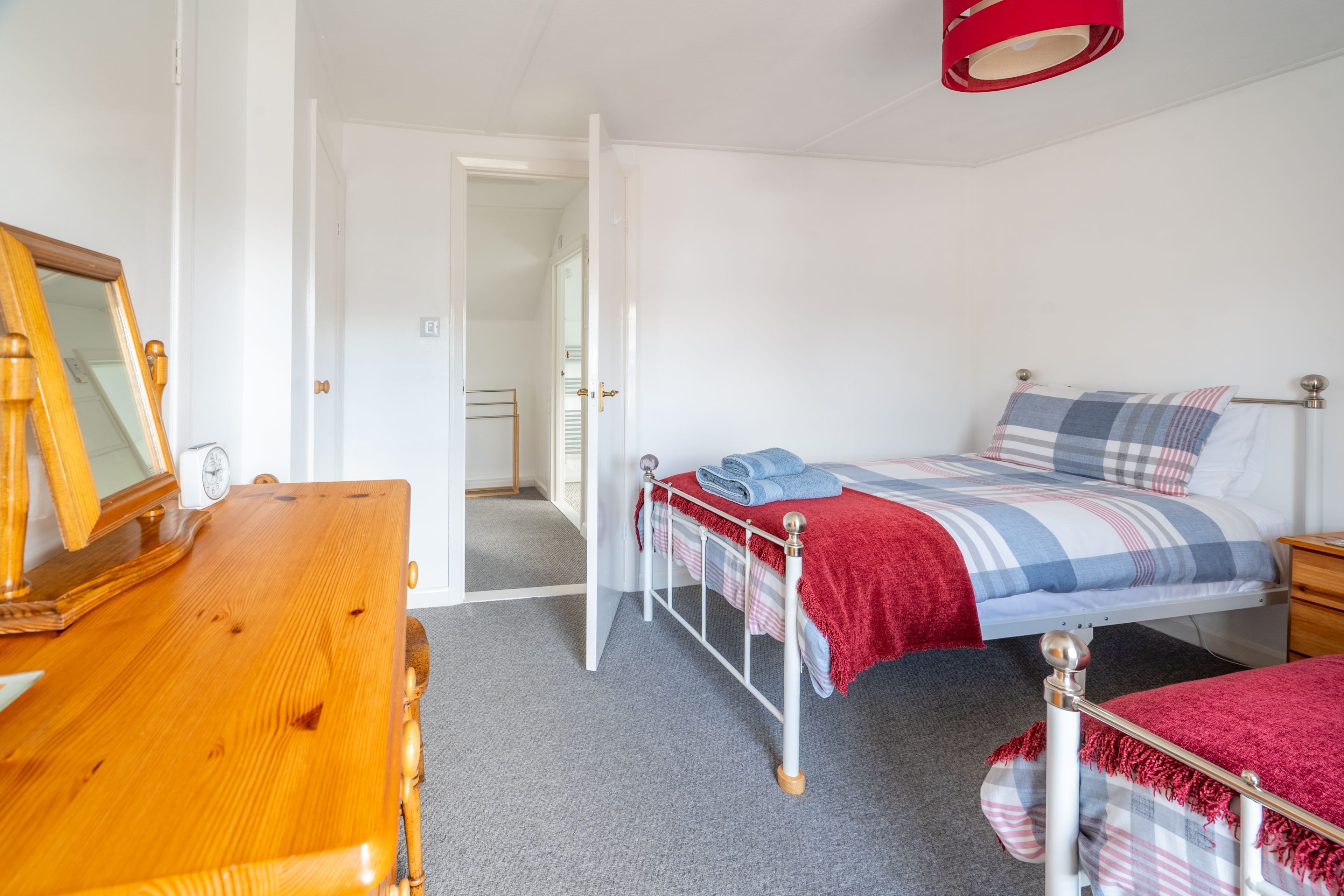 Ein Schlafzimmer mit einem Bett, einer Holzkommode, einem Spiegel und einer roten Lampe.