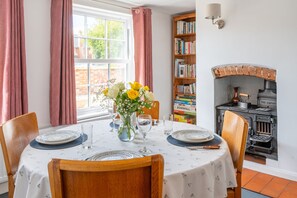 A dining area with a table set for four, a bookshelf, and a fireplace. - The Town House, Hollesley (Woodbridge)