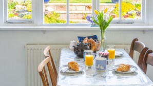 Een ontbijttafel met croissants, een vaas met bloemen, een theepot en uitzicht op een tuin door het raam.
