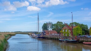 Een rustige rivier met boten afgemeerd aan een steiger, omringd door huizen en begroeiing.