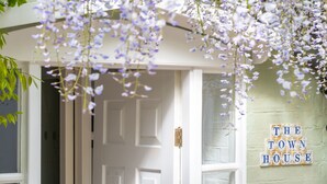 Een deuropening met een witte deur, een bordje met de tekst 'THE TOWN HOUSE' en paarse bloemen die eraan hangen.
