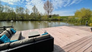 A wooden deck with outdoor seating and a view of a calm lake. - Water Villa in Ooltgensplaat Near Volkerak (Ooltgensplaat)