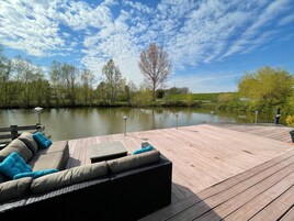 Um deck de madeira com área de estar externa e vista para um lago calmo.