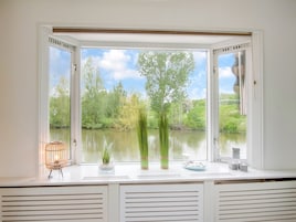 Quarto com uma grande janela com vista para a água e vegetação.