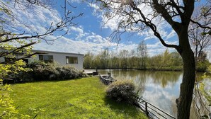 A lakeside property with a grassy lawn, a dock, and a house with large windows. - Water Villa in Ooltgensplaat Near Volkerak (Ooltgensplaat)