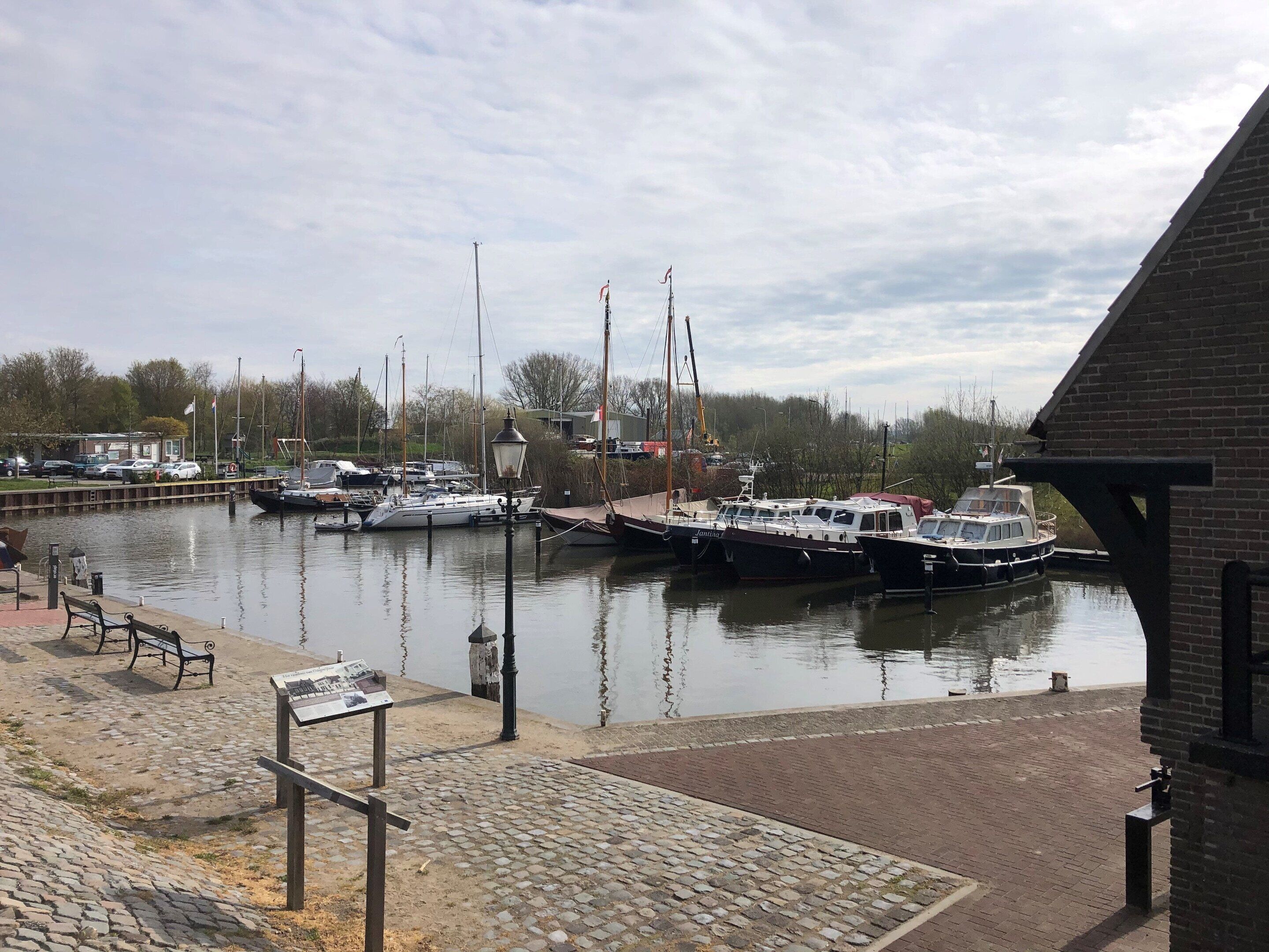 A marina with boats docked, a brick building, and a paved walkway with benches.