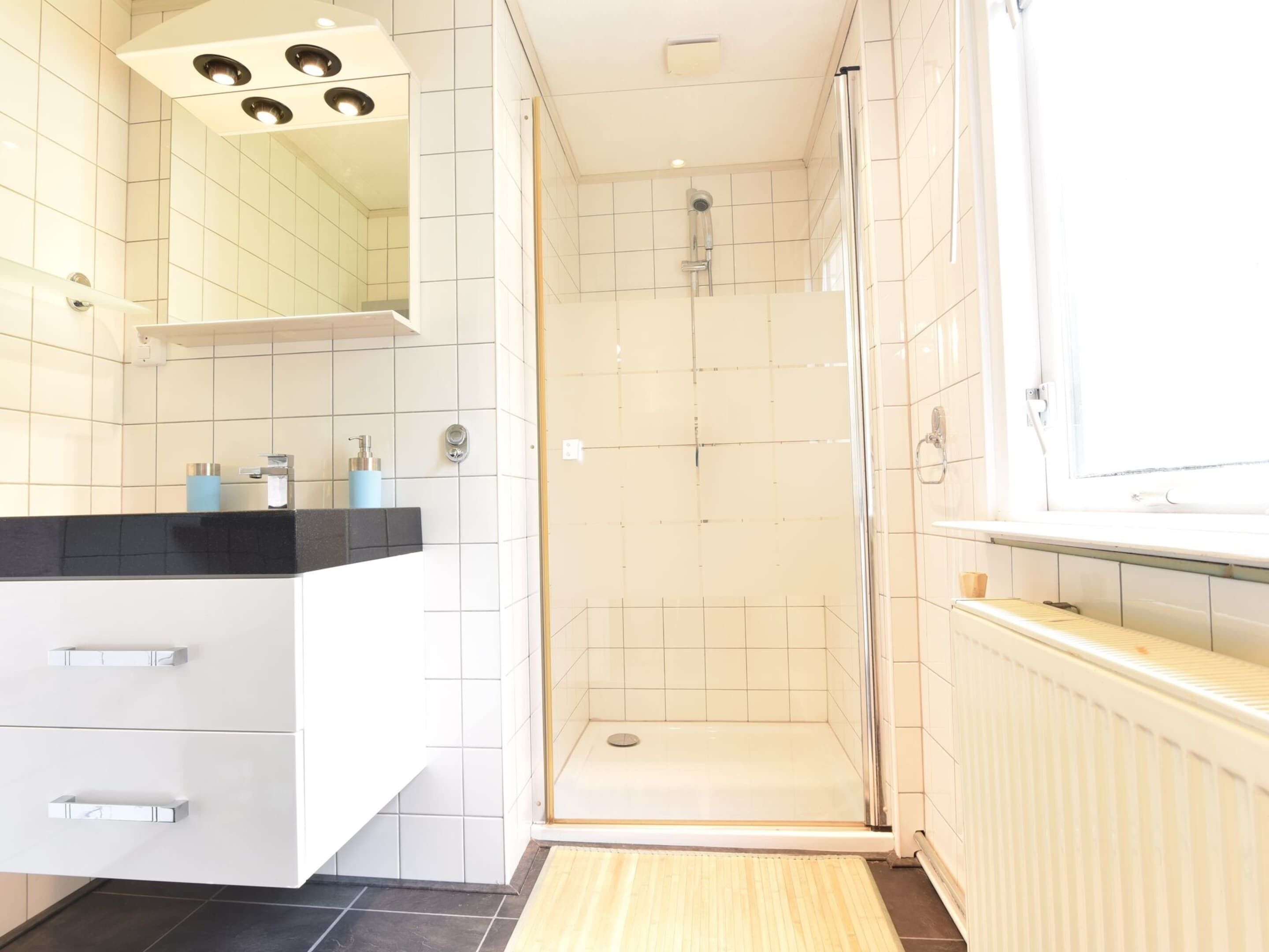A modern bathroom with a shower, a sink with a mirror, and a window.
