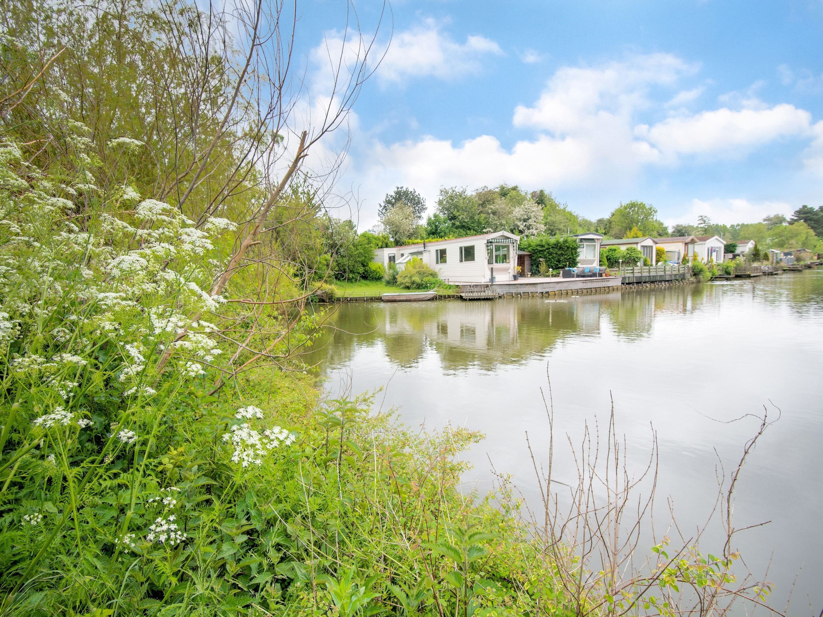 Une propriété située au bord de la rivière, comprenant une petite maison et un quai, entourée d’une végétation luxuriante et bordée d’un plan d’eau paisible.