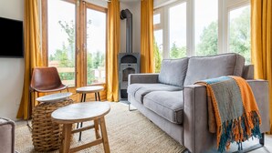 A cozy living room with a grey sofa, a small round table, a wicker stool, and a fireplace. - Idyllic Holiday Home in Ooltgensplaat on the Water (Ooltgensplaat)