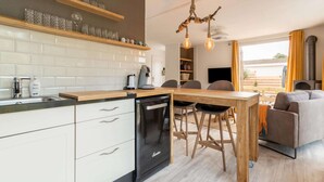A modern kitchen with white cabinets, a dishwasher, and a wooden dining table with chairs. - Idyllic Holiday Home in Ooltgensplaat on the Water (Ooltgensplaat)