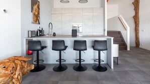 A modern kitchen with a central island, bar stools, and a staircase leading to an upper level. - Spacious Luxury Apartment With Beautiful Views of the Harbor and the North Sea (Ouddorp)