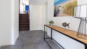 A hallway with a wooden console table, a fish decoration, and a painting of a beach scene. - Spacious Luxury Apartment With Beautiful Views of the Harbor and the North Sea (Ouddorp)