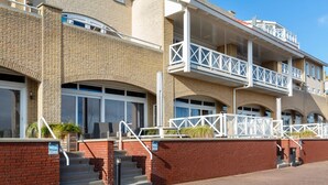A multi-story building with brick walls, white railings, and a staircase leading to the entrance. - Spacious Luxury Apartment With Beautiful Views of the Harbor and the North Sea (Ouddorp)