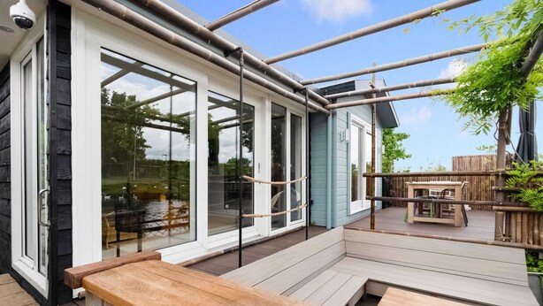A modern outdoor deck with glass doors leading to a patio area, a wooden bench, and a table. - Idyllic Holiday Home in Ooltgensplaat With Private Terrace (Ooltgensplaat)