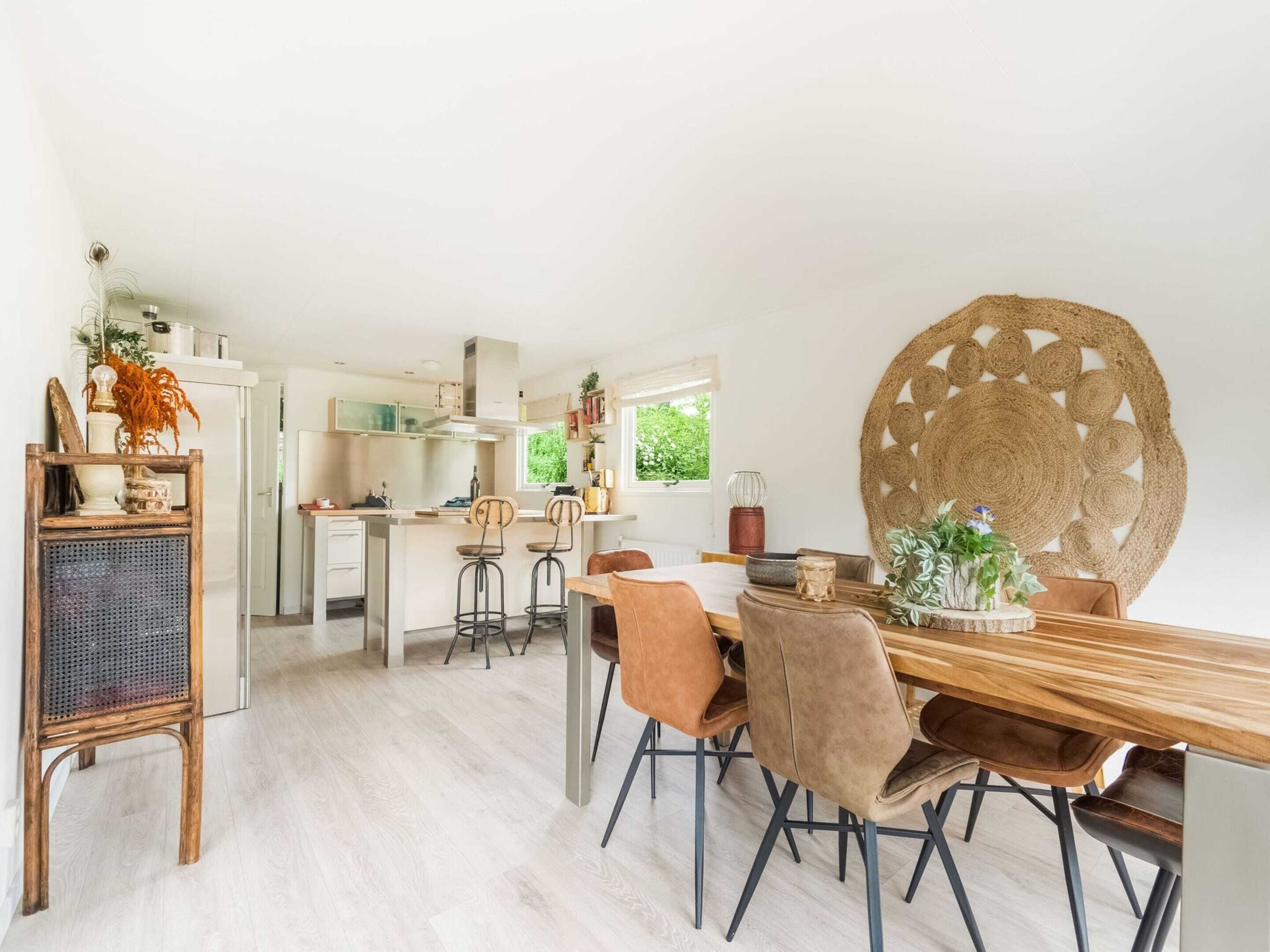 A modern kitchen with white cabinets, a wooden dining table with four chairs, and a large woven wall hanging.