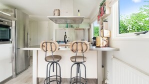 A modern kitchen with two bar stools, a built-in oven, and a window with a view of greenery. - Idyllic Holiday Home in Ooltgensplaat With Private Terrace (Ooltgensplaat)