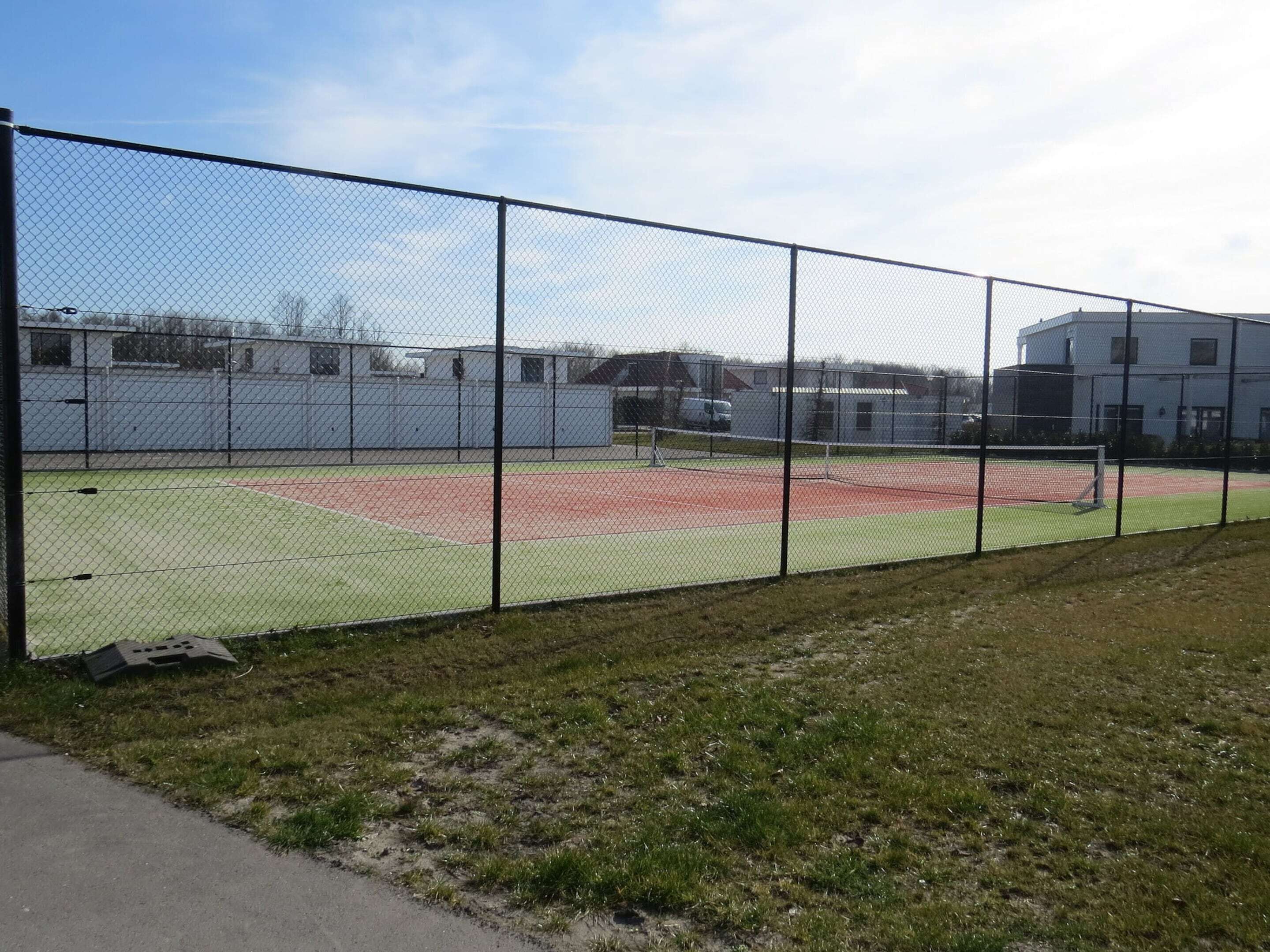 A fenced sports field with a green playing area and a red track.
