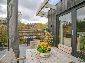 Eine Terrasse im Freien mit einem Holztisch, Stühlen, einem Grill und einem Blumentopf.