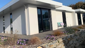 A modern building with large glass doors and windows, a stone retaining wall, and a small outdoor seating area. - Villa in Harderwold With Garden (Zeewolde)