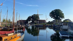 A marina with boats docked, a windmill, and buildings in the background. - Villa in Harderwold With Garden (Zeewolde)