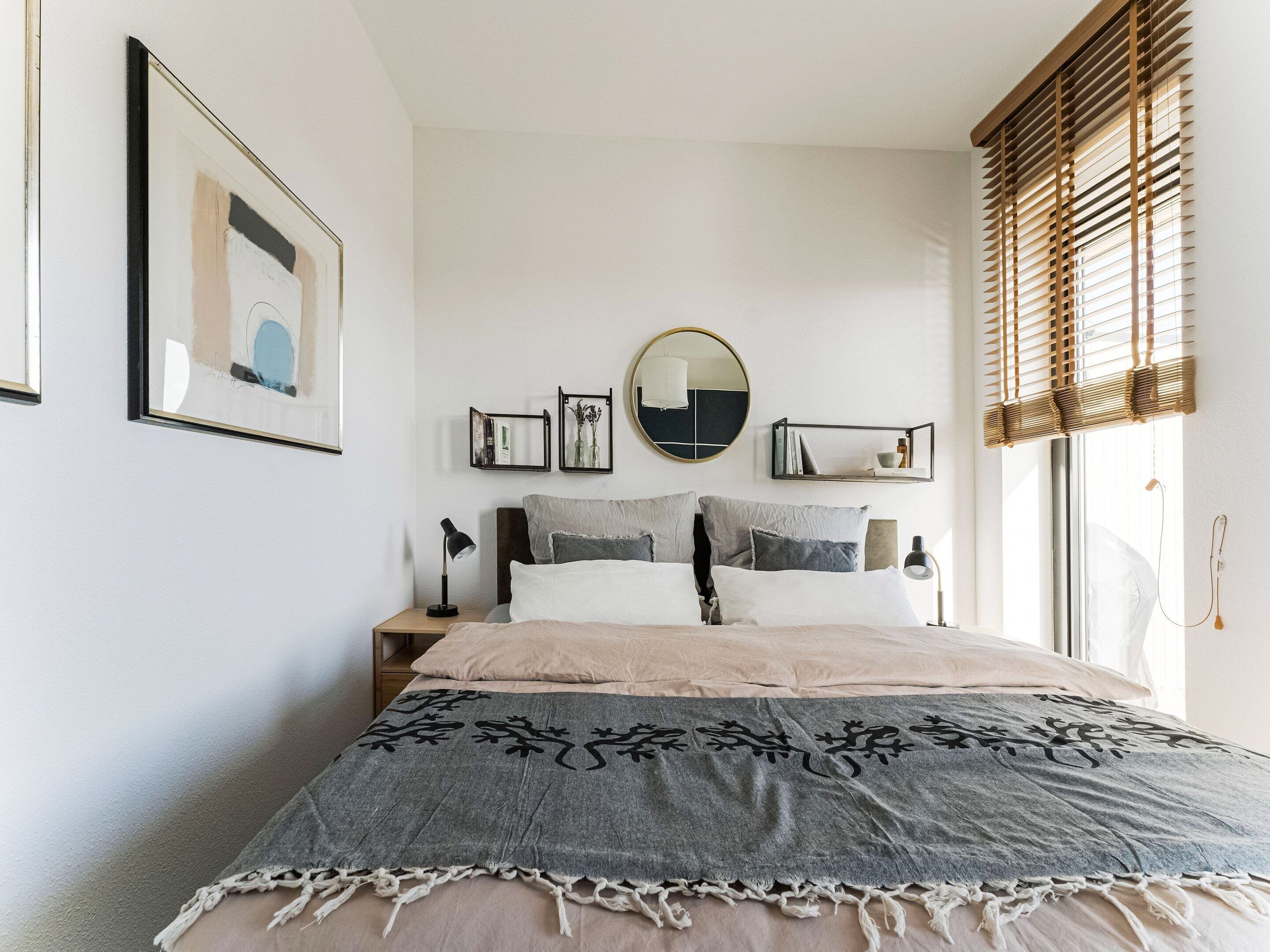 Ein Schlafzimmer mit Bett, Nachttischen, einem Spiegel und einem Fenster mit Jalousien.