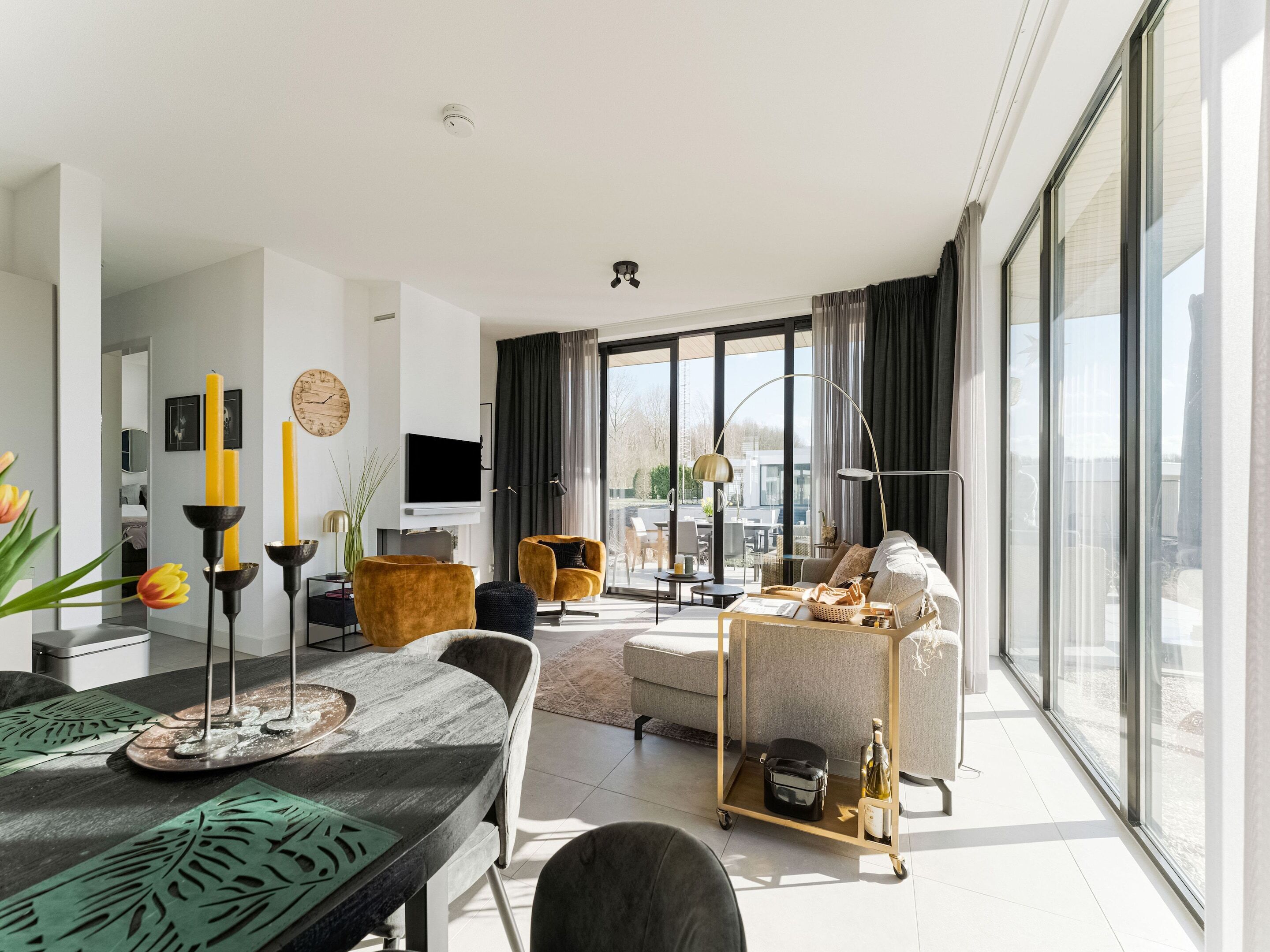 A modern living room with a large window, a flat-screen TV, and a dining area with a table and chairs.