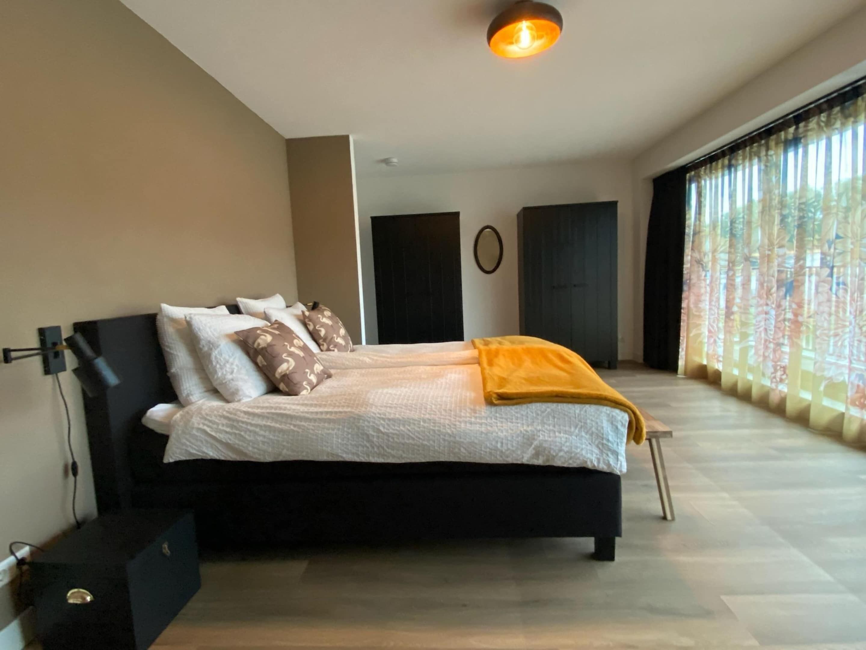 Een moderne slaapkamer met een zwart bed, wit beddengoed en een gele plaid.