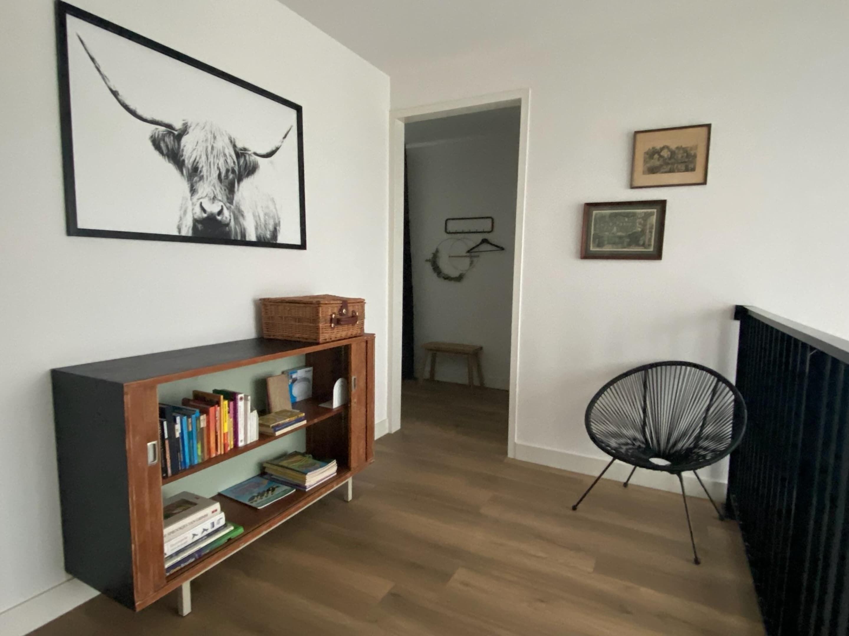 A hallway with a wooden bookshelf, a framed bull picture, a black chair, and a small bench.