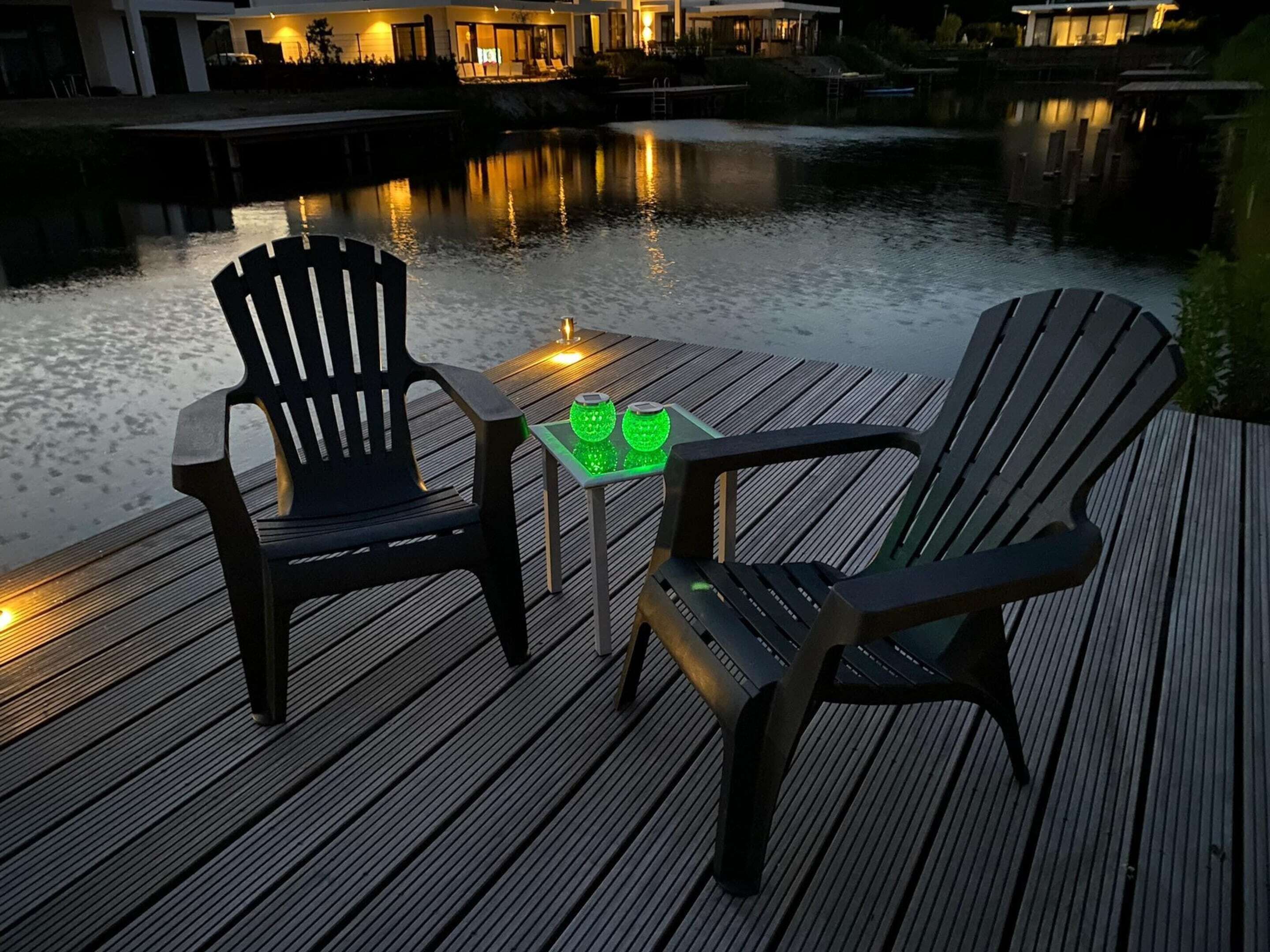 Une terrasse en bois avec deux fauteuils Adirondack et une petite table agrémentée de deux objets décoratifs verts.