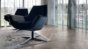 Una habitación moderna con una silla azul oscuro, un tapiz estampado y cortinas de gasa con diseños florales.