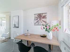 A dining area with a wooden table, black chairs, a vase of flowers, and a framed picture on the wall.